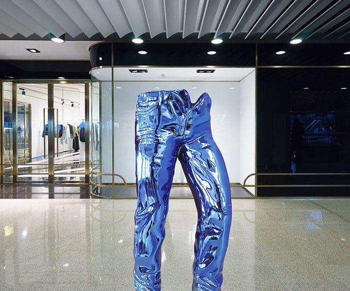 Small Decorative Jeans Resin Sculpture 1 A reflective blue sculpture of jeans on display in a modern indoor gallery.