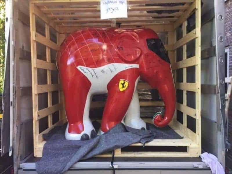 Ferrari Elephant sculpture 3 Sztuczny słoń pomalowany w kolorach Ferrari, umieszczony w drewnianej skrzyni transportowej.