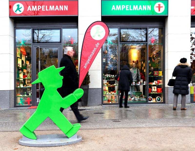 oryg_064490685_1129949550544944_1465385417682452480_o Storefront of an Ampelmann shop with a large green walking man figure in front and pedestrians passing by.