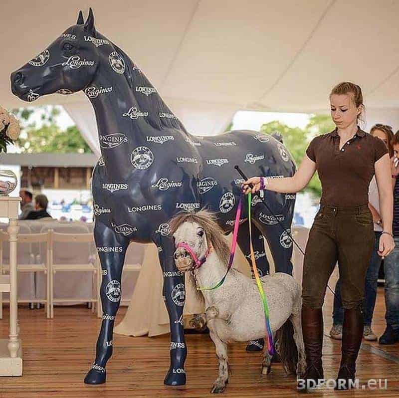 oryg_064490685_1129949550544944_1465385417682452480_o A woman holding a miniature horse in front of a large horse statue covered with
