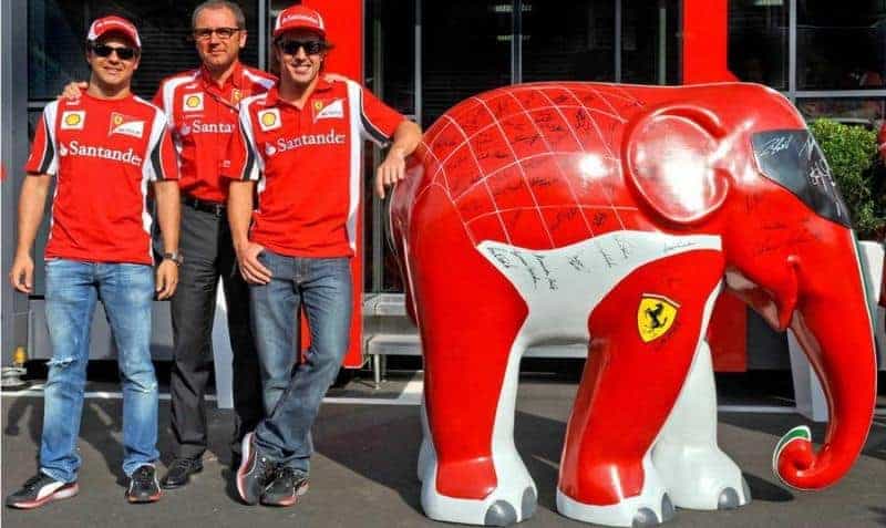 oryg_064490685_1129949550544944_1465385417682452480_o Three men in Ferrari team shirts posing beside a red and white elephant statue with signatures and Ferrari logos.