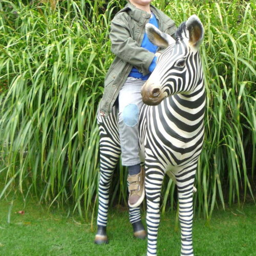 A child sits on a zebra sculpture in front of tall grass.