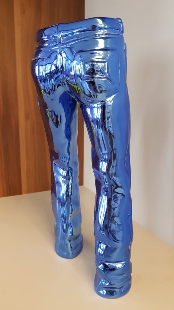 Small Decorative Jeans Resin Sculpture 4 Chrome blue sculpture of the lower body wearing jeans, displayed indoors against a wooden and white background.