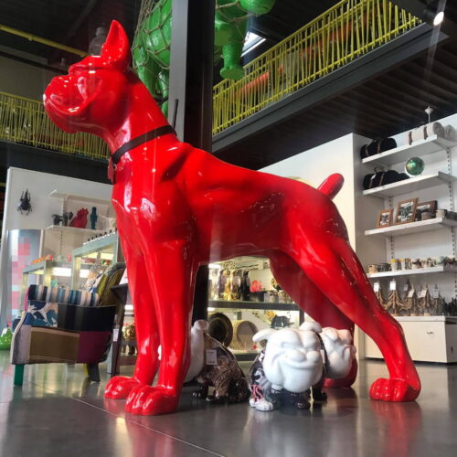 A large red dog sculpture in a modern store with various art pieces, including a green rhinoceros hanging from the ceiling.