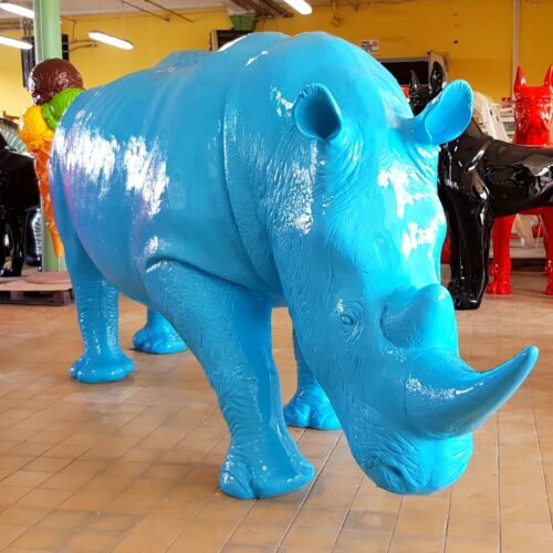 Large, colorful animal sculptures in a room, including a blue rhinoceros in the foreground and red and black canines in the background.