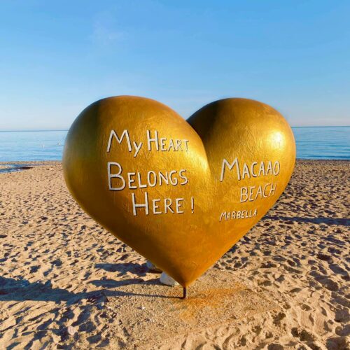 Large golden heart sculpture on the beach with the text 
