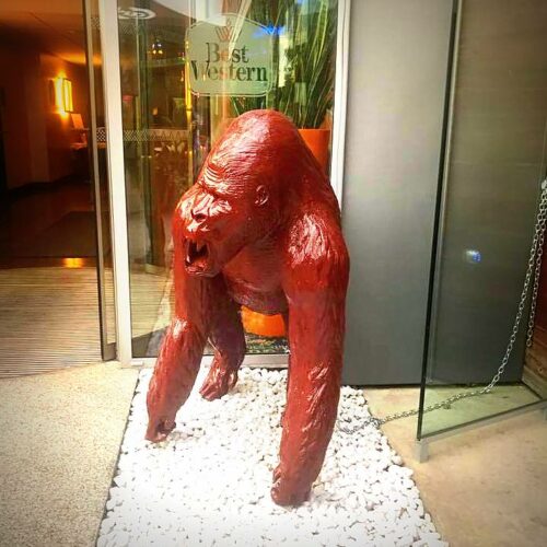 A red gorilla statue at the entrance of a Best Western hotel, standing on a bed of white stones.