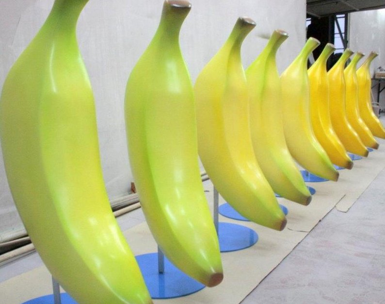 Realistic Large Banana Fiberglass Model 4 Large, colorful banana sculptures arranged in a row on blue stands.