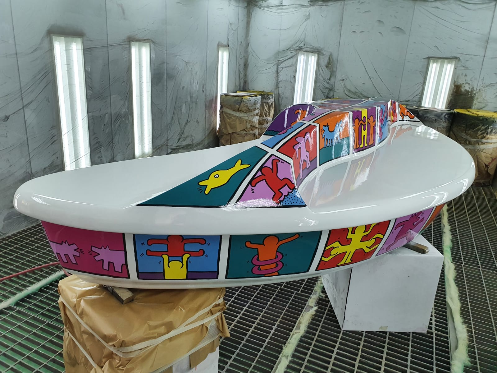 Shopping center fiberglass bench 4 White boat with colorful, geometric patterns and abstract figures, inside a workshop with bright lighting.
