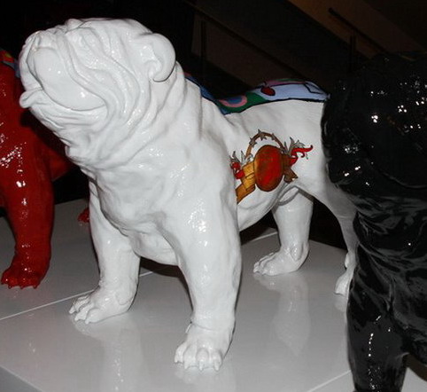 Statue of a white bulldog with colorful decorations on its side, standing on a pedestal.