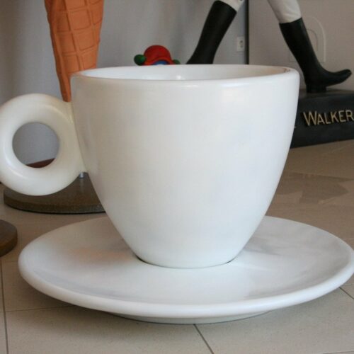 Oversized white teacup and saucer on a tiled floor with giant ice cream cone and mannequin legs in the background.