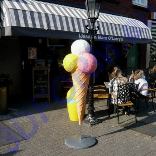 Large ice cream cone sculpture outside a striped awning ice cream shop with people sitting at outdoor tables.