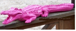 A bright pink alligator sculpture displayed on a wooden surface.