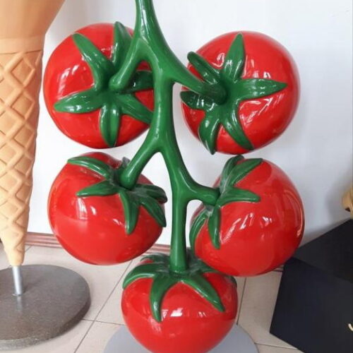 A sculpture of a tomato vine with five large, red tomatoes, positioned next to a giant ice cream cone sculpture.