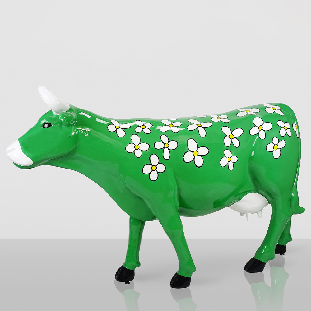 Fiberglass Cow Life Size Statue - Single Color 3 Green cow sculpture with white horns and black hooves decorated with white flowers with yellow centers on its body, standing on a reflective surface against a plain light background.