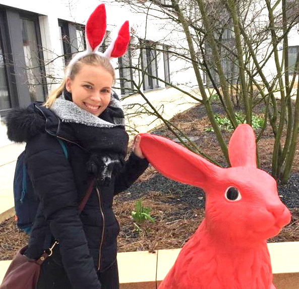 Large Rabbit Fiberglass Statue - Single Color 5 A woman wearing red and white bunny ears headband stands next to a large red rabbit sculpture outdoors.