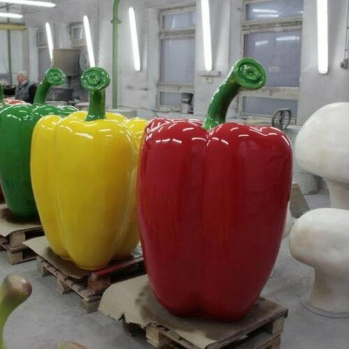 Oversized sculptures of red, yellow, and green bell peppers and large mushrooms in an industrial workshop.