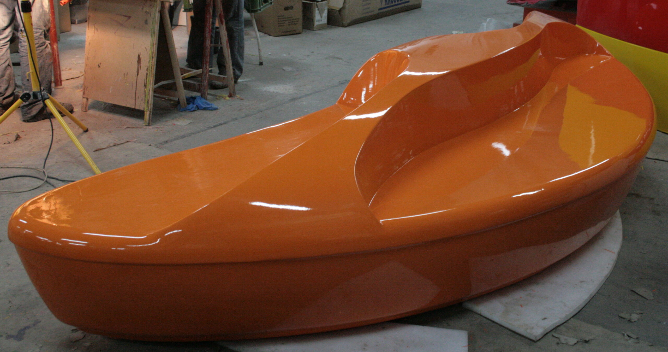 Shopping center fiberglass bench 5 A shiny orange mold of a sleek, aerodynamic vehicle or boat hull placed on a workshop floor.