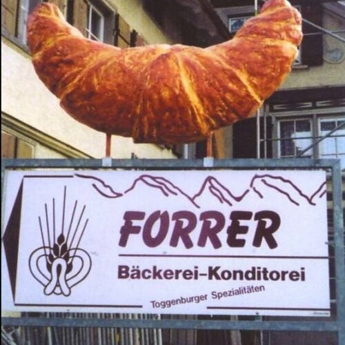 Sign for Forrer Bakery and Pastry Shop in Toggenburg, featuring a large croissant sculpture on top.