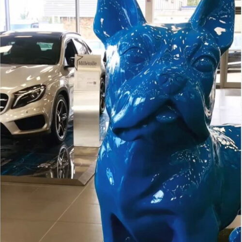 Large blue dog statue in a car showroom with a white vehicle displayed in the background.