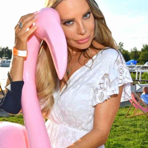 Woman in a white dress posing with a pink inflatable flamingo in an outdoor setting.