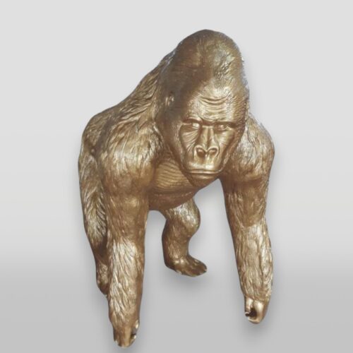 Gold-colored sculpture of a gorilla in a walking pose.