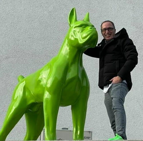 Man smiling and posing with a large green dog statue.