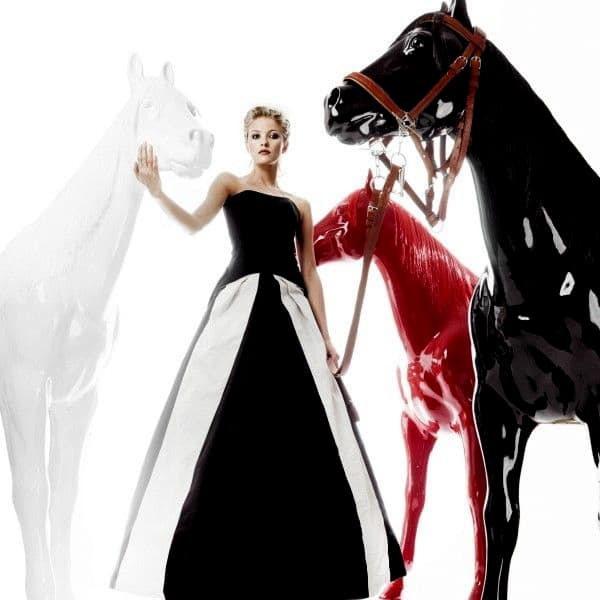 Fiberglass horse figure with a mane 1 Woman in a black and white gown standing among three large, decorative horse figures in black, white, and red colors.