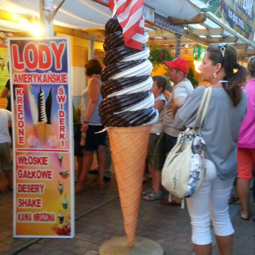 A large plastic ice cream cone statue with swirled chocolate and vanilla, standing outside a booth with a sign advertising 