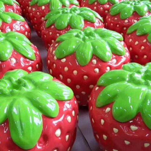 Large shiny artificial strawberries with bright green leaves arranged closely together.