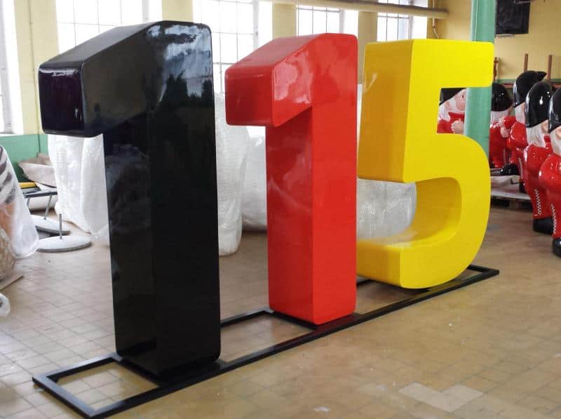 Large 3D Numbers 4 Czarno-czerwono-żółte rzeźby liczb 1, 1 i 5 na stalowej podstawie w pomieszczeniu.