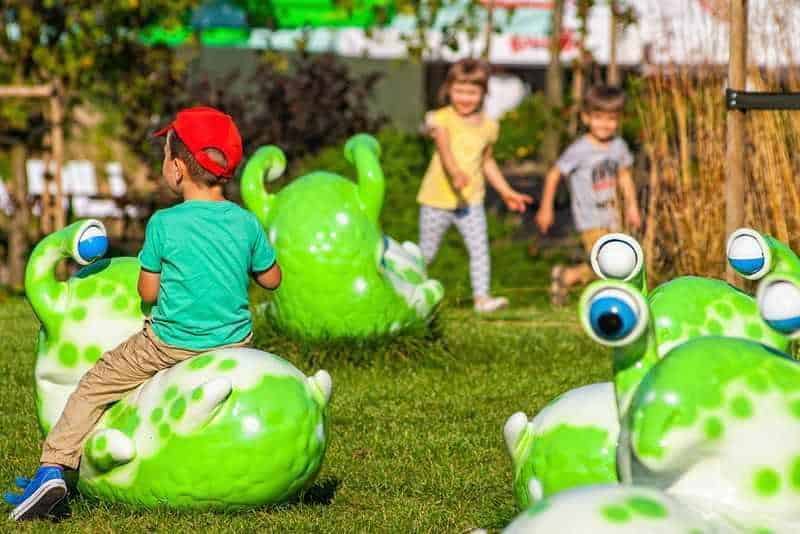 Children playing on large green snail sculptures in an outdoor playground.
