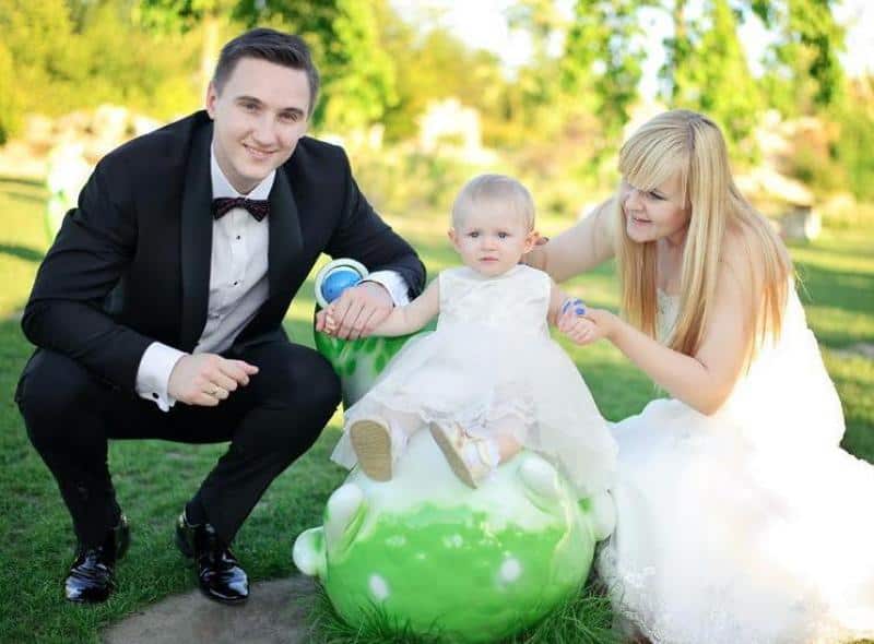 Mężczyzna w garniturze i kobieta w sukni ślubnej z małym dzieckiem na świeżym powietrzu.