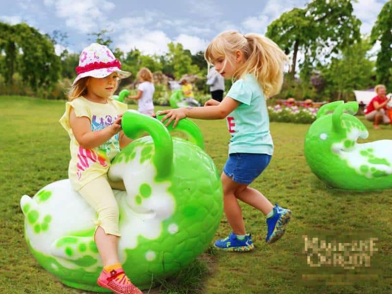 Dzieci bawiące się na zielonym trawniku z kolorowymi, zielono-białymi, dużymi zabawkami w kształcie ślimaków.