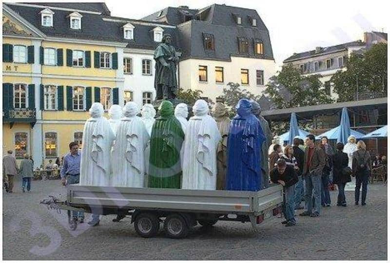 Replica of the Beethoven Monument 2 Grupa kolorowych rzeźb na przyczepie na placu miejskim, budynki w tle.