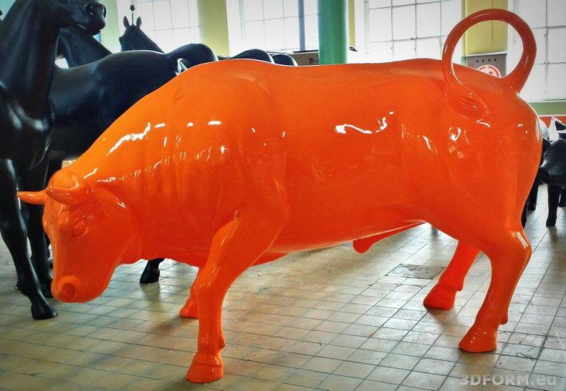Large event bull figure 1 Pomarańczowa rzeźba byka znajdująca się w środku, na tle czarnych rzeźb koni