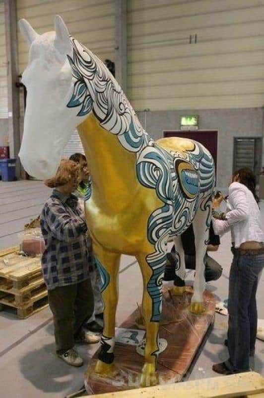 Large figures painted by children 3 Ludzie malujący dużą rzeźbę konia w budynku.
