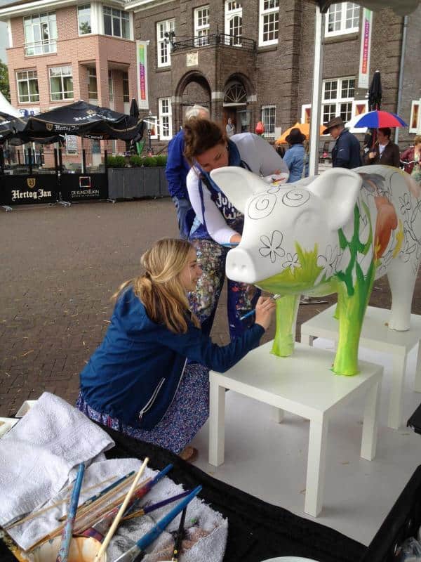 Large figures painted by children 1 Kobiety malują wielką rzeźbę krowy na zewnątrz budynku.