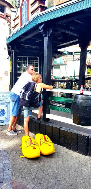 Para osób w żółtych, dużych drewnianych butach pozuje do zdjęcia przed budynkiem w stylu holenderskim.