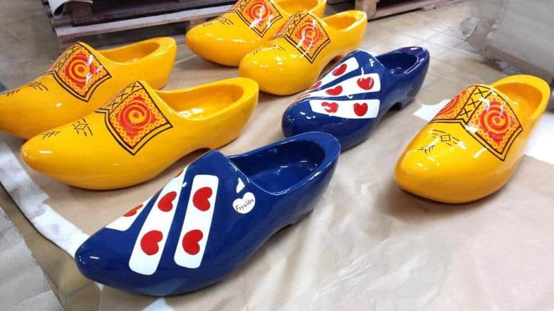 Colorful oversized wooden clogs, painted in vibrant yellow and blue with decorative patterns, lying on a surface.