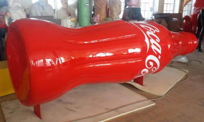 Coca-Cola advertising truck 2 Duża rzeźba w kształcie butelki Coca-Coli w czerwonym kolorze, znajdująca się w warsztacie.