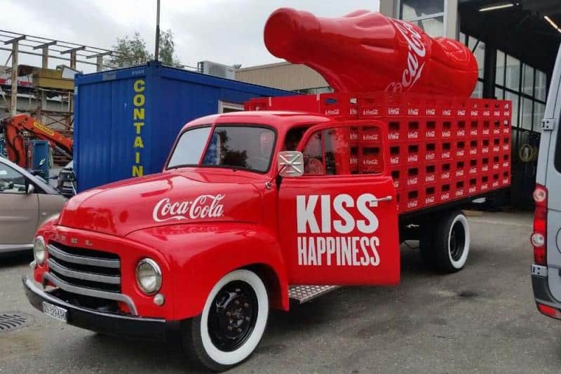 oryg_064490685_1129949550544944_1465385417682452480_o A vintage red Coca-Cola truck with a large bottle on the back and the words