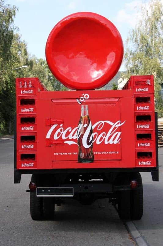 Coca-Cola advertising truck 4 Tył czerwonej ciężarówki promującej Coca-Colę z dużą butelką i logo marki.