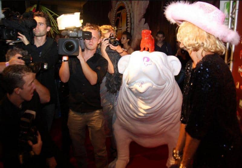 Large bulldog figure 2 Kobieta w różowym kapeluszu pozuje na czerwonym dywanie obok dużej, białej rzeźby psa, otoczona przez fotoreporterów.