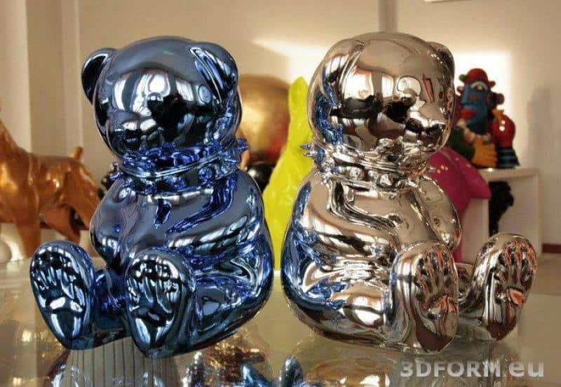 Dwie błyszczące figurki misiów, jedna w kolorze niebieskim, druga srebrna, stojące na szklanej powierzchni.