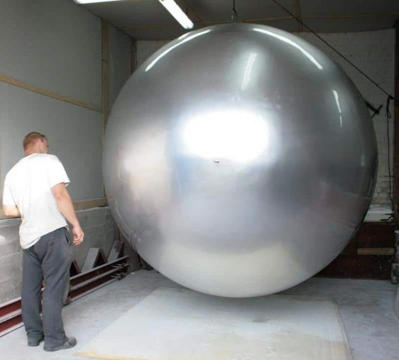 Giant Sphere in Urban Space 4 Mężczyzna stojący obok ogromnej, srebrnej kuli w hangarze.