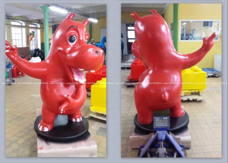 oryg_064490685_1129949550544944_1465385417682452480_o Red cartoon hippo sculpture with outstretched arms, seen from front and back, placed indoors on a wooden pallet.