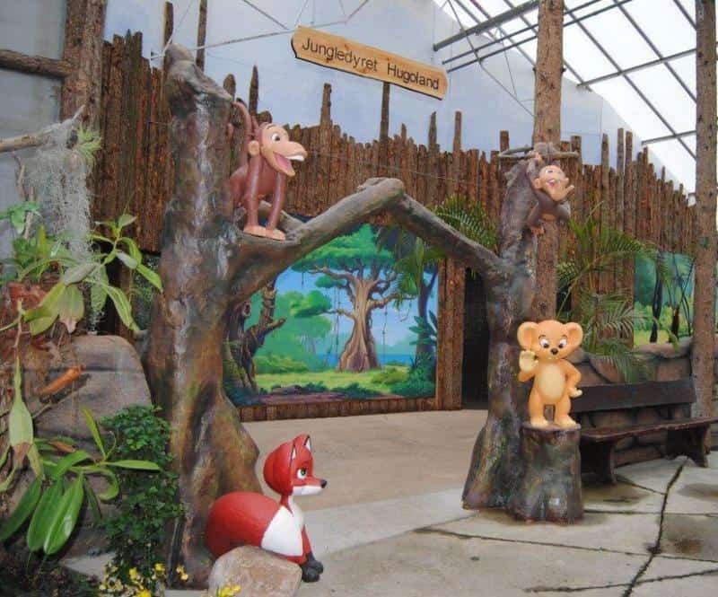 oryg_064490685_1129949550544944_1465385417682452480_o Wooden archway with cartoon animal statues, including a monkey, fox, and lion cub, under a sign reading