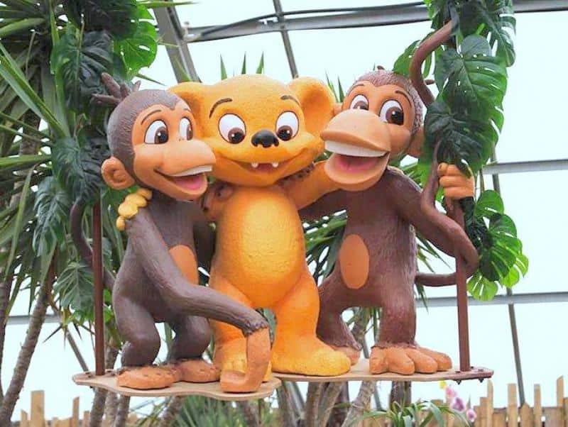 Figures for amusement park - Hugo Land 2 Trzy postacie kreskówkowe: dwa małpy i jeden stwór o pomarańczowej sierści, stoją razem na huśtawce w otoczeniu roślin.