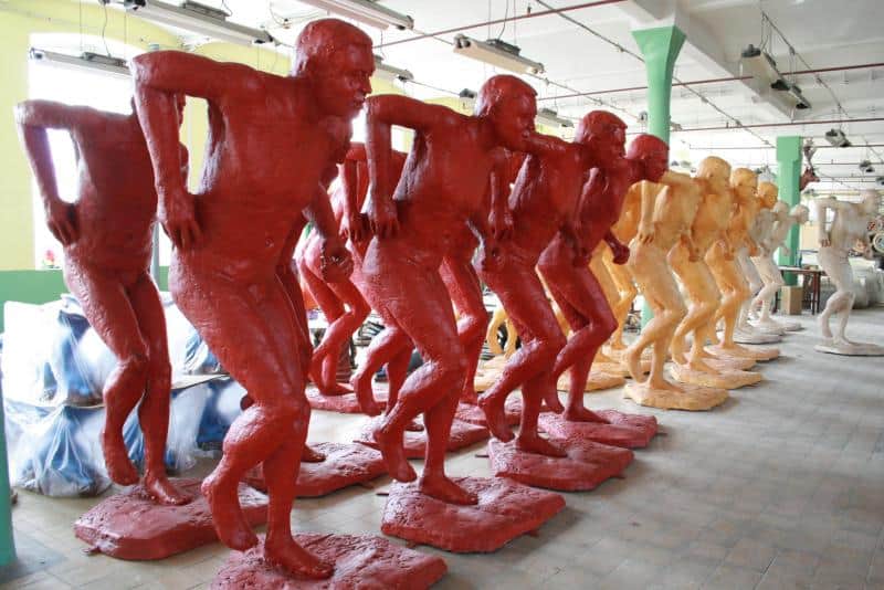 IAAF World Championships Promotion 2 Figury męskich postaci w dziwnie wykręconej pozie, pomalowane na czerwono, pomarańczowo i biało, ustawione w rzędzie w przestrzeni magazynowej.